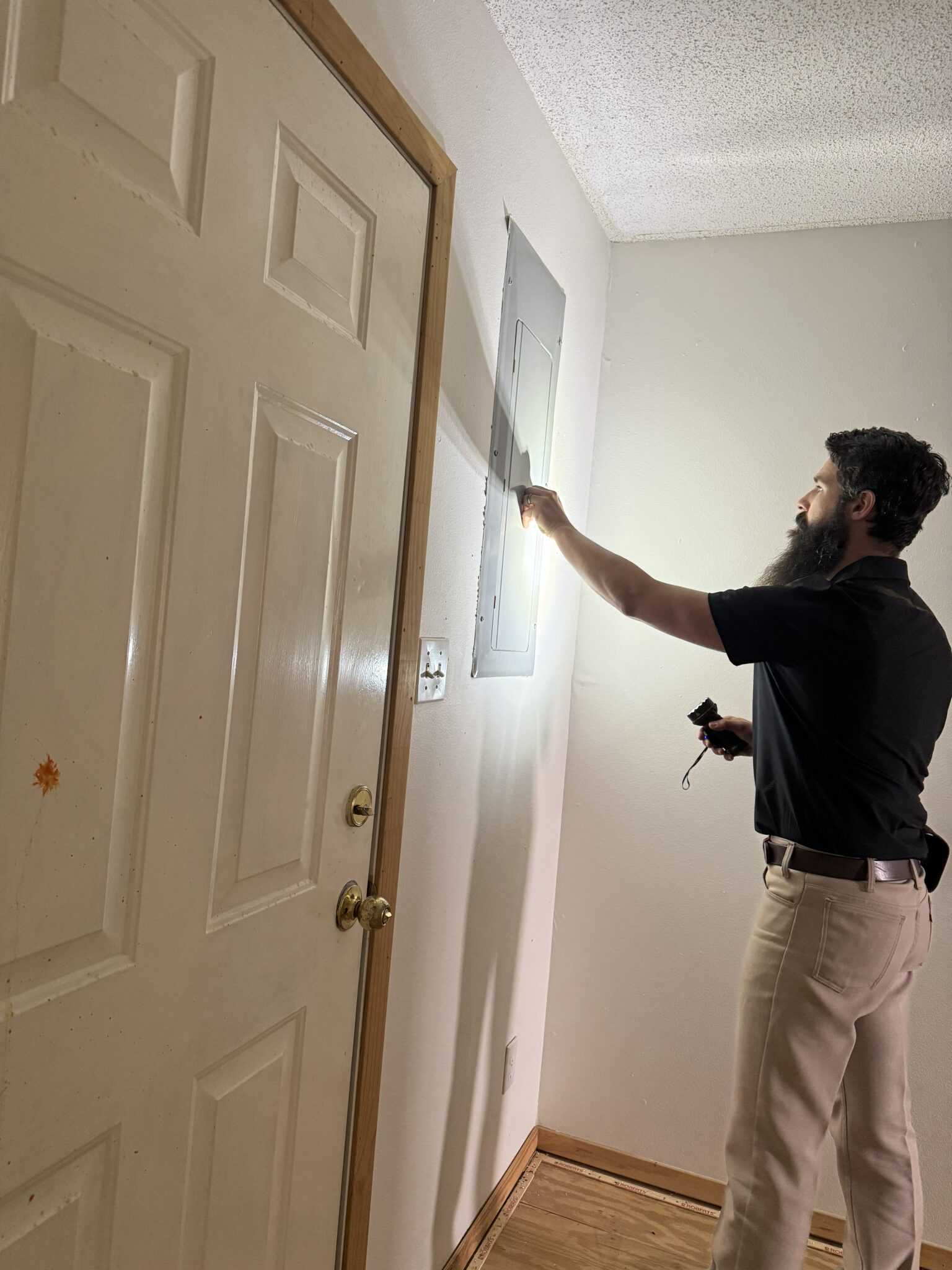 Home inspector preparing to inspect an electrical service panel with a flashlight in East Texas.