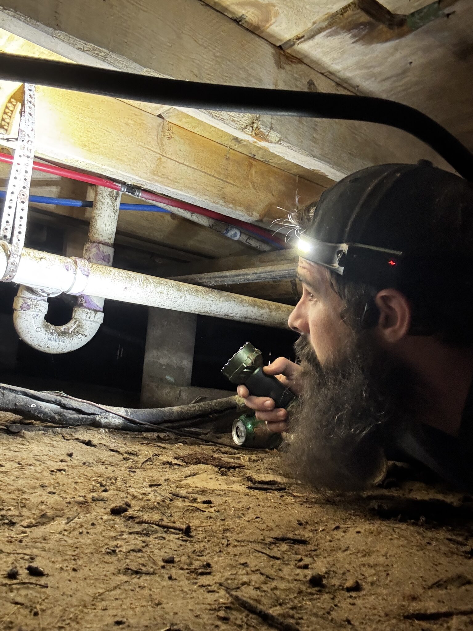 Home inspector in crawl space examining foundation and plumbing